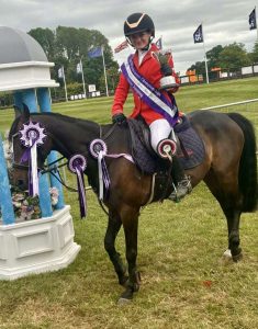 Equestrian rider holding trophy on decorated horse with rosettes after show jumping win